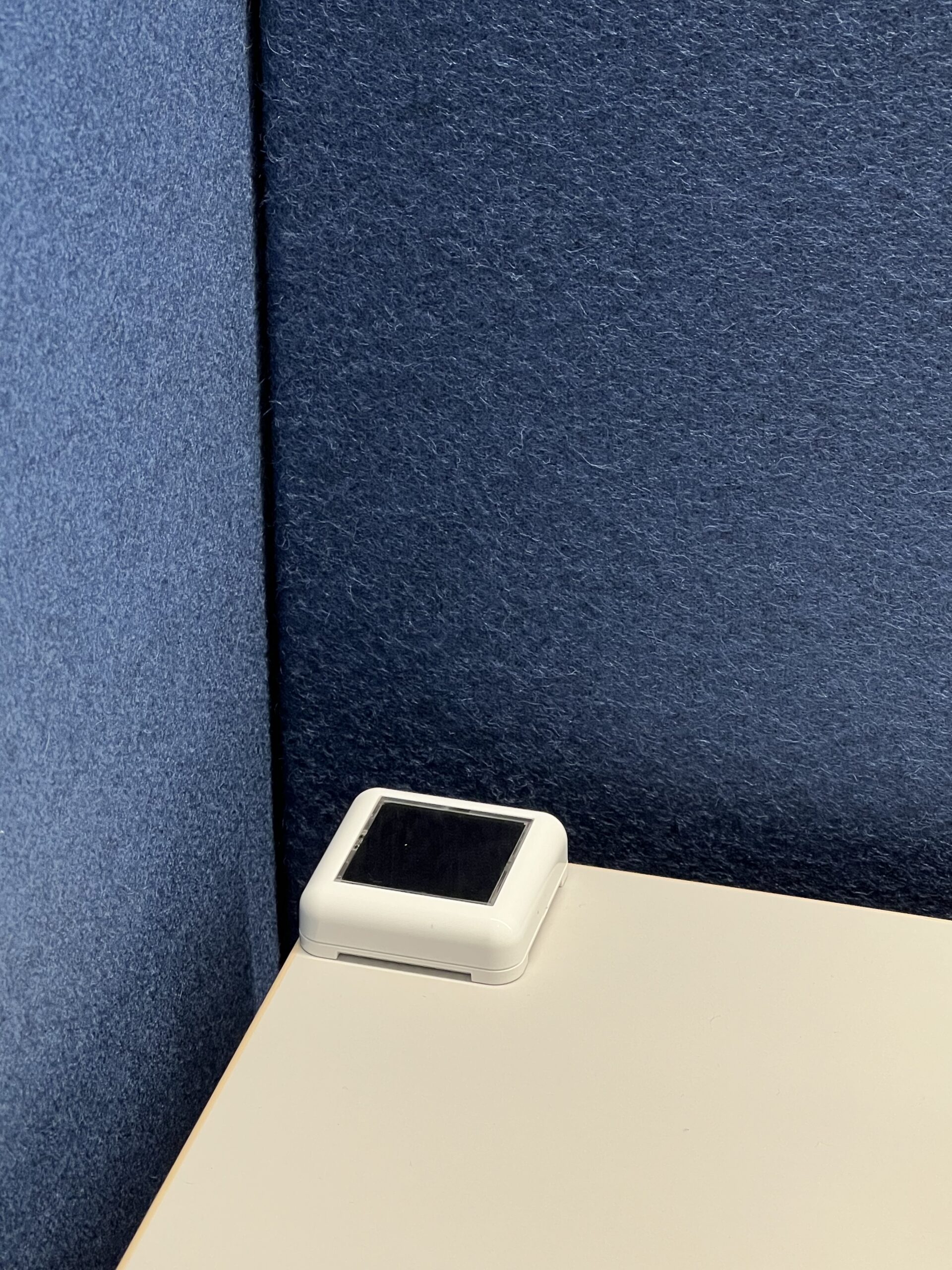 EnoSense® WALL+DESK im weissen Gehäuse montiert auf einer Schreibtsichplatte in der linken oberen Ecke